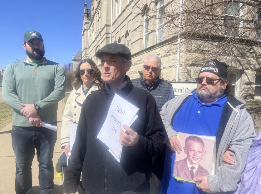 SNAP Missouri Director David Clohessy, middle front, speaks outside of the Spalding Pastoral Center in downtown Peoria. He's surrounded by victims of child sex abuse and their families, who asked not to be identified by name. Some carry photos of children at the age when they were abused. Collin Schopp