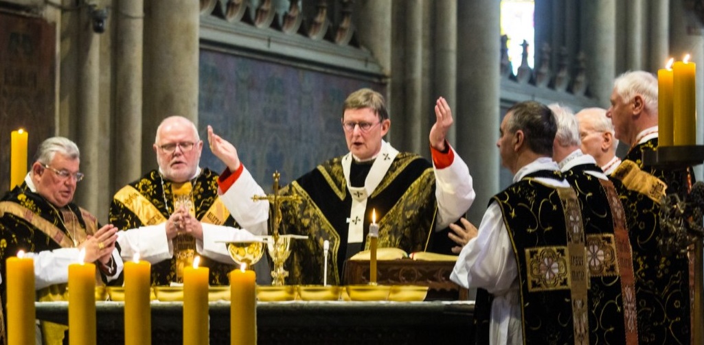 Cardinal Woelki, with his hands raised, presides over the 2017 funeral Mass of Cardinal Joachim Meisner. Woelki and his fellow concelebrants are seen as a byproduct of the "Ratzinger system." Photo: Raimond Spekking via Wikimedia Commons. @ upload.wikimedia.org/wikipedia/commons/6/60/Exsequien_Joachim_Meisner-7747.jpg,